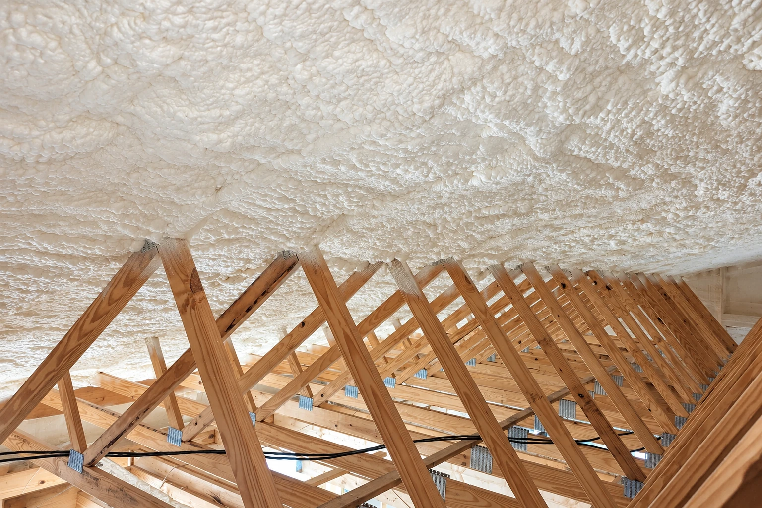 Exposed roof trusses beneath a ceiling coated with white spray foam insulation.