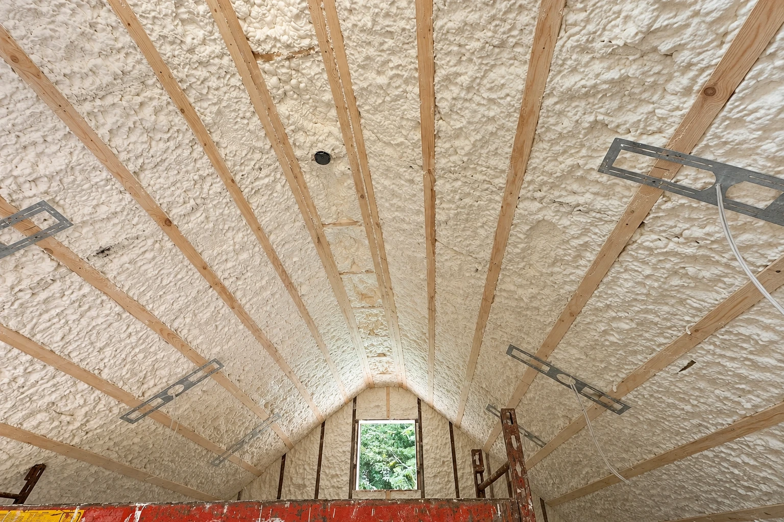 White spray foam insulation fills the sloped roof between exposed wooden rafters.