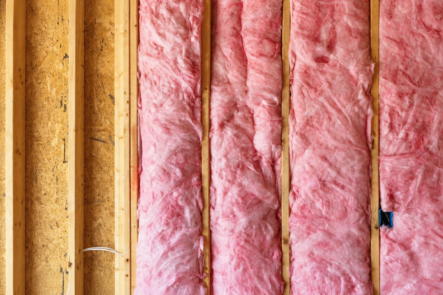 Pink fiberglass batts fill the spaces between exposed wooden wall studs.
