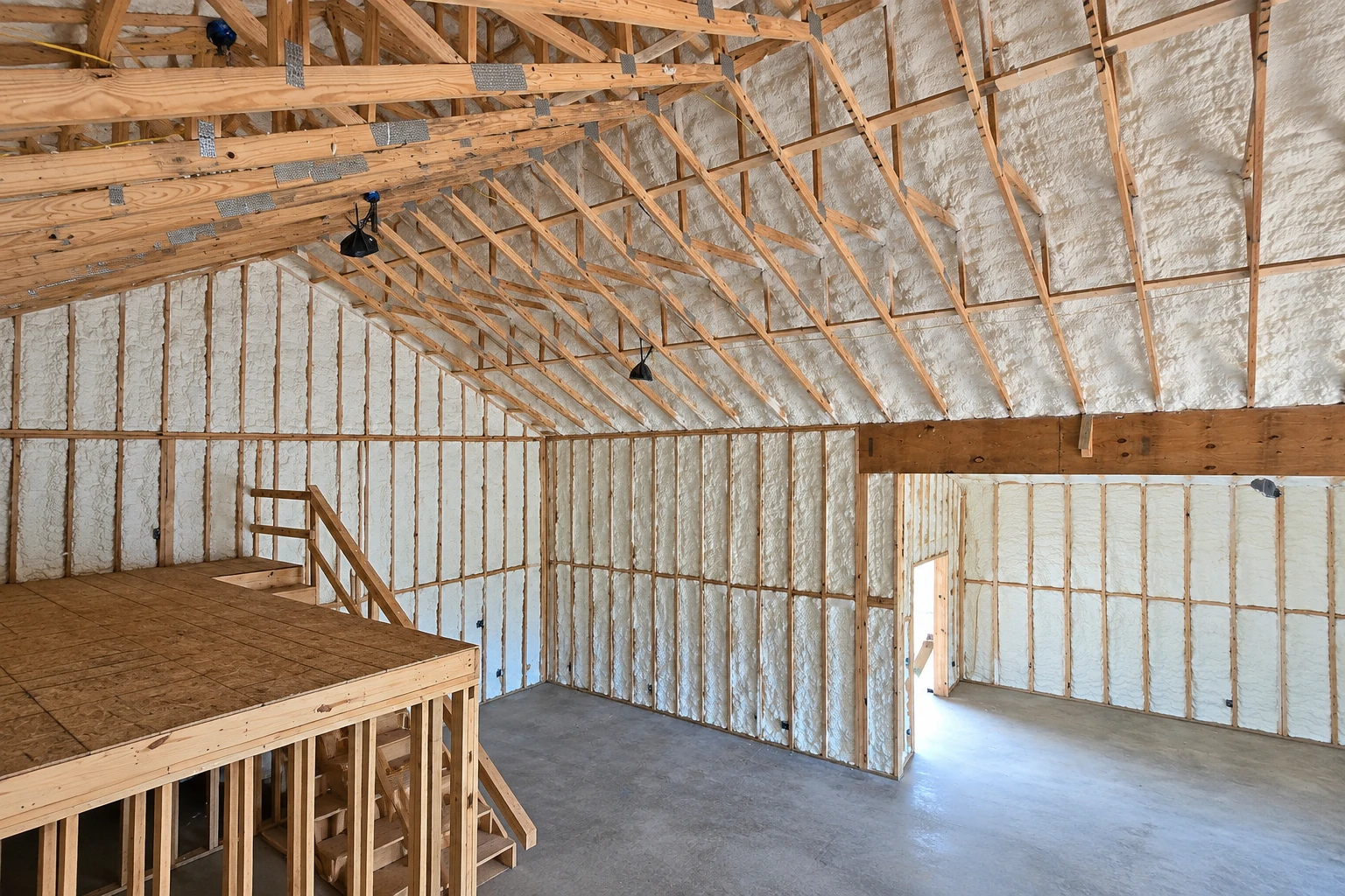 An unfinished timber-framed room has white spray foam insulation filling the wall and roof cavities.
